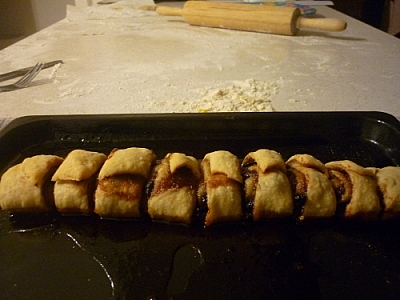 Baked pastries cooling on a cooking sheet, the countertop in the background covered in flour, a wooden rolling pin completing the scene.