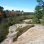 A scenic view of a pink granite rock outcrop rising above an autumn forest in the background.