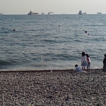 Children playing on a rocky beach with ships on the horizon, a water hose leading to the ocean from an unseen beach restaurant where ethical eating and vegetarian living in Korea is made that much easier.