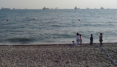 Children playing on a rocky beach with ships on the horizon, a water hose leading to the ocean from an unseen beach restaurant where ethical eating and vegetarian living in Korea is made that much easier.