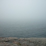 Thick fog hovering above Georgian Bay from Red Rock Point, almost completely hiding the water from view.