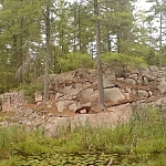 A pink rock outcrop topped with conifers rises over a barely visible body of water.