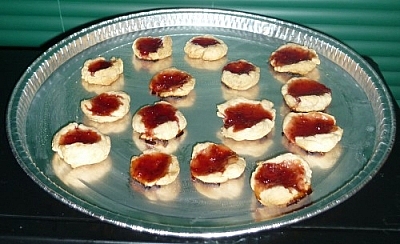 Jam cookies, a few of them with some bright red filling oozing out onto the baking sheet.