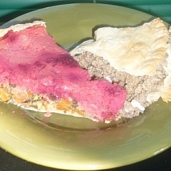 A slice of mixed veggie pie with mashed potato and red beet top crust, and a slice of meat pie, both siting on a small side plate.