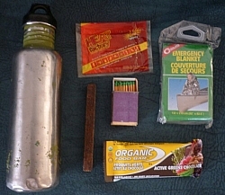 Emergency winter gear (clockwise from left): water bottle, hand warmer, emergency blanket, protein bar, fire starter, waterproof matches.