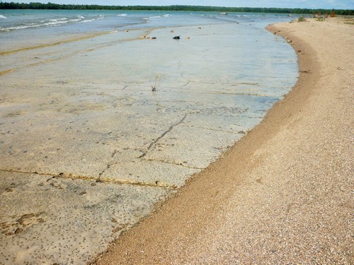 The ebb and flow of waves reveals alvar pavement beneath the sand at Misery Bay.