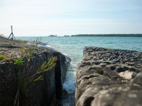 Waves crash through a crevice in coastal rocks covered with pit karren.